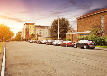 old concrete road near building in sunny day. many cars parking on the side of road.