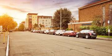old concrete road near building in sunny day. many cars parking on the side of road.