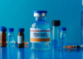 closeup of a simulated vial of fentanyl on a blue table next to a syringe and some other different vials