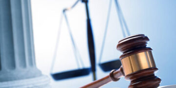 A gavel rests on top of an open law book with a justice scale and a Greek column in the background.
