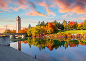 Vivid fall colors of red, orange, and yellow at the Spokane Washington Riverfront Park along the Spokane River with the Great Northern Clock Tower in view. Spokane is a city in eastern Washington state.