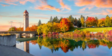 Vivid fall colors of red, orange, and yellow at the Spokane Washington Riverfront Park along the Spokane River with the Great Northern Clock Tower in view. Spokane is a city in eastern Washington state.